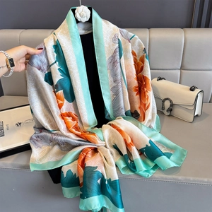 Elegant satin scarf with peony floral print in cyan and orange hanging on display