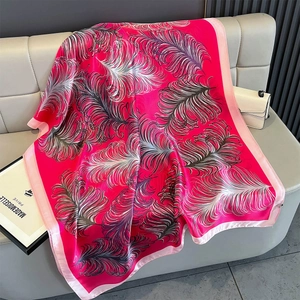Detail of rose red feather print silk scarf draped on a grey leather background