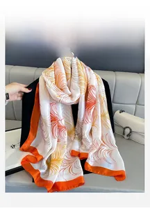 Detail of satin silk scarf featuring orange feather prints and bright contrast border