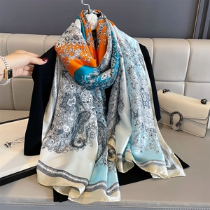 Silk-like paisley scarf in orange and blue draped over a black blazer on a sofa