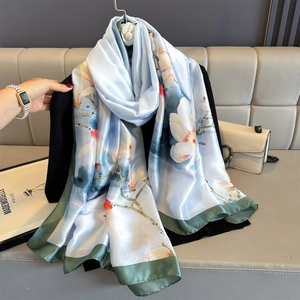 Light blue floral silk scarf with magnolia print and green border hanging elegantly