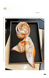 Detailed view of cream and orange floral silk scarf on a luxury black display tray