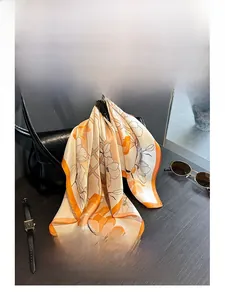 Detail of floral silk scarf in orange and beige tied as an accessory on a black leather bag