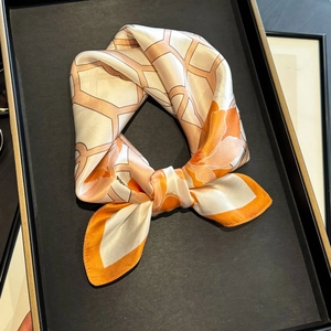 Elegant silk scarf with orange floral prints and geometric patterns on a black display tray