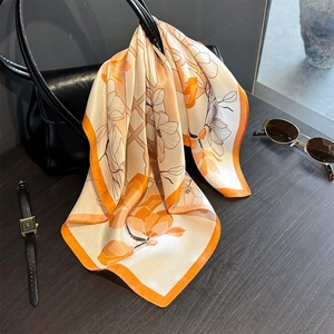 Floral print silk scarf with orange borders draped over a black leather handbag