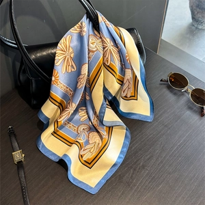 Silk-like square neck scarf with geometric patterns draped on a black leather handbag