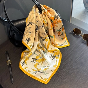 Seidenquadrattuch mit Blumenmuster in Gelb und Orange an einer schwarzen Handtasche