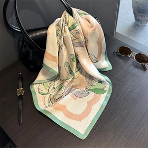 Silk magnolia print square scarf draped over a black bag with premium smooth texture