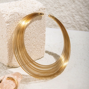 Golden multi-layer wire collar necklace and earrings set on white stone background