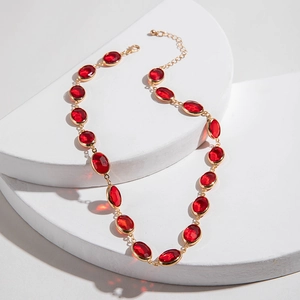 Dettaglio della collana dorata con gemme rosse ovali su espositori geometrici bianchi
