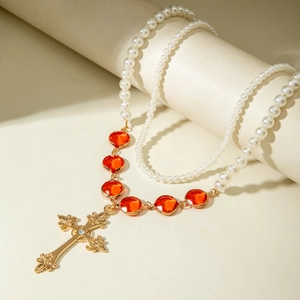 Dettaglio di una collana di perle con gemme rosse e ciondolo a croce dorata sul supporto
