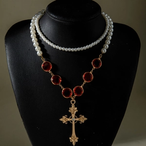 Dettaglio di collana a strati con perle, pietre rosse e pendente a croce barocca dorata