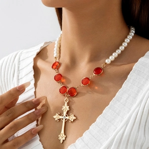 Dettaglio del ciondolo a croce dorata con perle rosse e bianche sulla collana