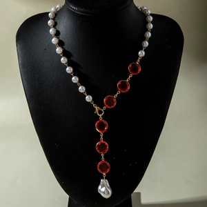 Dettaglio macro di gemme rosse e ciondolo con perla barocca su collana dorata