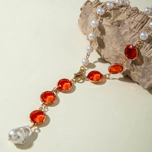 Dettaglio della collana dorata con pietre preziose rosse e ciondolo in perla barocca