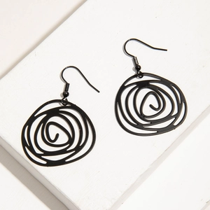 Detail view of minimalist black irregular swirl pendant earrings on a white surface.