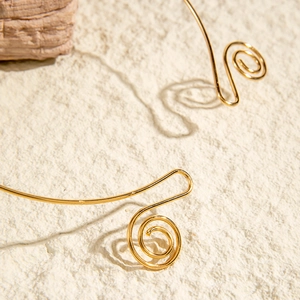 Detail of vintage gold metal choker featuring double spiral curls on sandy texture