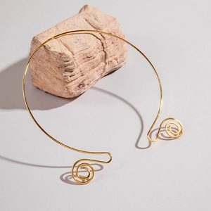 Macro detail of golden spiral wire choker resting on a beige textured stone accessory