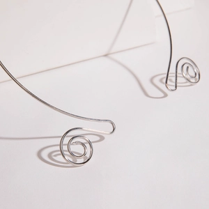 Macro detail of silver spiral metal collar necklace featuring elegant curved wire design