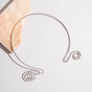 Detailed view of silver metallic choker with elegant spiral ends on a textured stone
