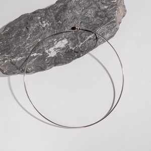 Minimalist silver metal collar necklace with spherical hook clasp on dark stone surface