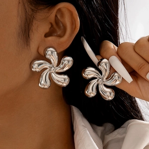 Gros plan de boucles d'oreilles fleur argentées surdimensionnées au fini miroir poli