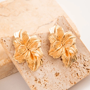 Détail de boucles d'oreilles dorées texturées en forme de fleur sur socle en pierre