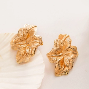 Détail de boucles d'oreilles feuilles dorées avec texture brossée sur un coquillage
