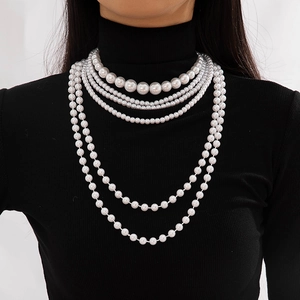 Detail of five-layered faux pearl necklace showing various bead sizes on black knitwear