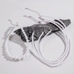 Close-up of layered faux pearl necklaces with silver clasps on a black natural stone background