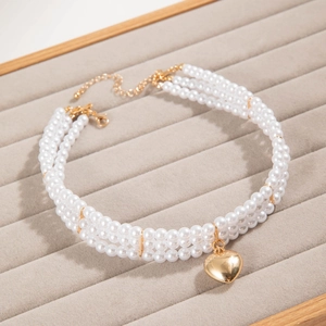 Macro shot of triple-layer pearl necklace featuring a polished golden heart pendant