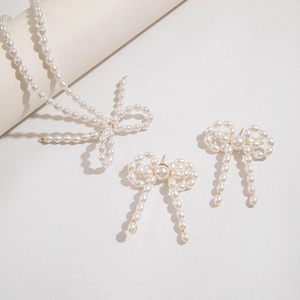 Dettaglio di un set di gioielli con perle, collana e orecchini a fiocco su sfondo minimalista