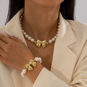Primo piano del set di collana e braccialetto di perle con ciondoli a fiocco dorato su modella