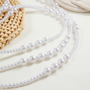 Detail of layered white pearl necklace with alternating bead sizes on a rustic straw mat