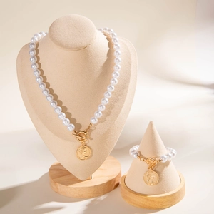 Dettaglio set collana e bracciale di perle con ciondolo a moneta d'oro e chiusura a T