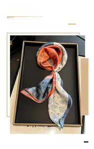 Detail of silk square scarf featuring orange and blue abstract patterns and a pearl buckle