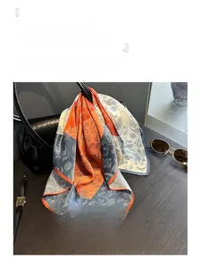 Close-up of lightweight paisley floral silk scarf styled on a leather handbag with sunglasses
