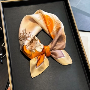 Silk neck scarf with orange floral and butterfly patterns on black display tray