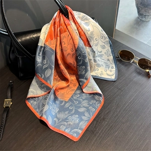 Silk-like floral scarf with orange and blue contrast draped on a stylish black handbag