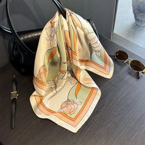 Elegant silk scarf with floral pattern and orange border draped over a black leather handbag