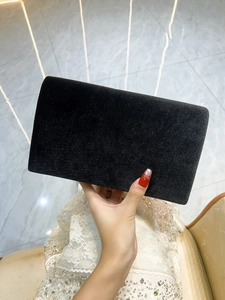 Close-up of a minimalist black velvet evening clutch held by hand against a lace dress