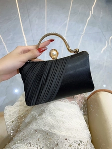 Detail of black satin evening clutch with gold handle, large pearl clasp and pleated fabric