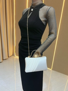 Close-up of white satin evening clutch featuring oversized pearl clasp and gold chain strap