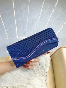 Detail of navy blue pleated evening clutch with rhinestone strap held against white lace