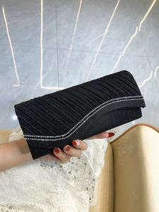 Detail of black pleated evening clutch featuring shimmering fabric and rhinestone chain