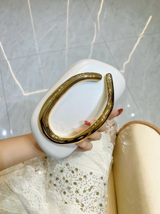 Detailed view of white evening clutch with a distinctive gold C-shaped metal handle