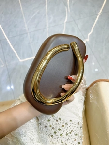 Detail of a brown leather clutch featuring a large circular gold metal handle and luxury finish