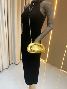 Close-up of gold pebble-shaped clutch with glitter texture and chain strap on velvet dress