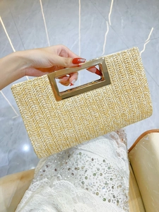 Close-up of woven straw clutch bag with golden metal handle and herringbone texture