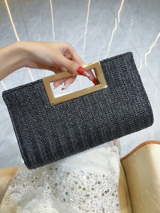 Detail of hand-held black straw clutch featuring a V-shaped weave and golden metal handle